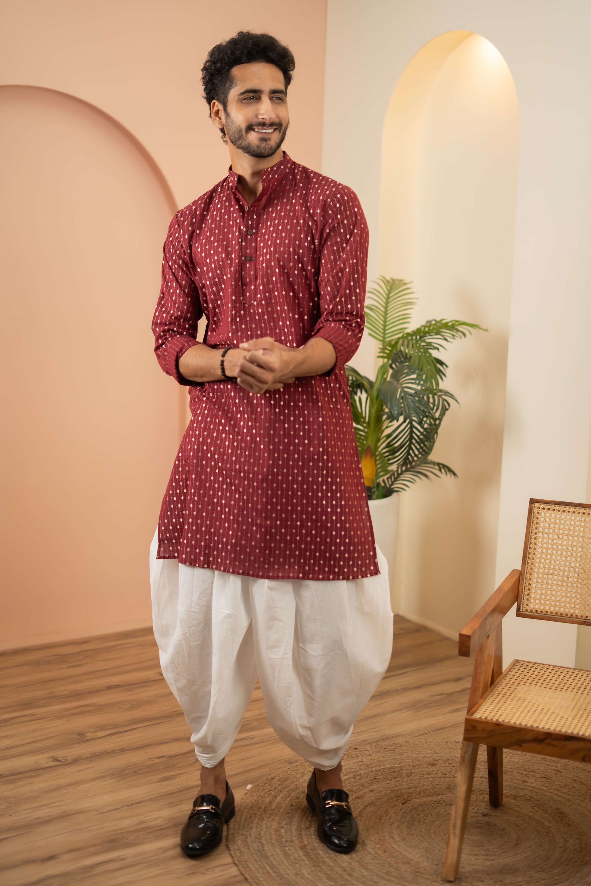 A man wearing a maroon kurta paired with a white dhoti, showcasing traditional attire and cultural elegance.