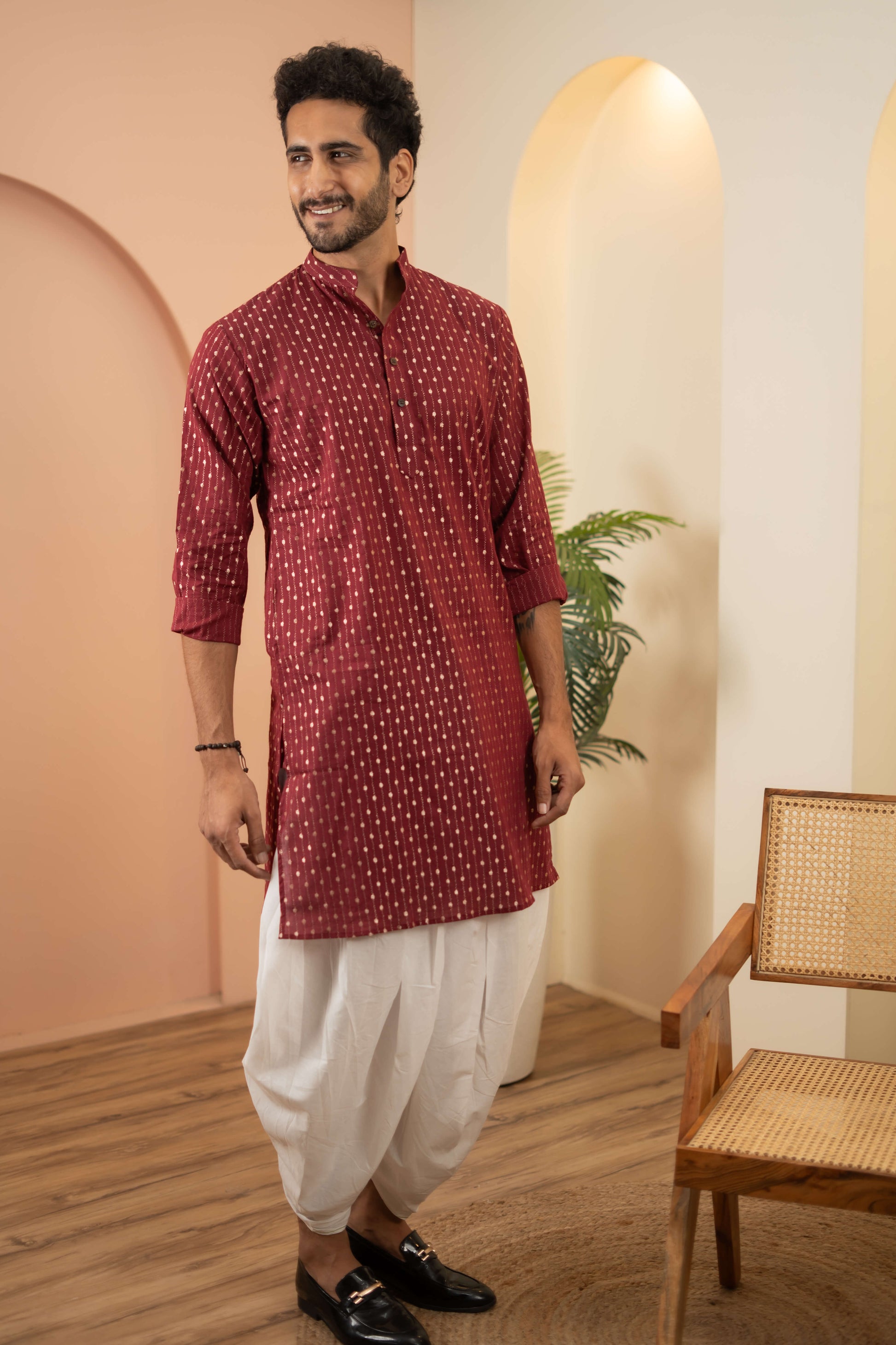 A man wearing a maroon kurta paired with a white dhoti, showcasing traditional Indian attire. 