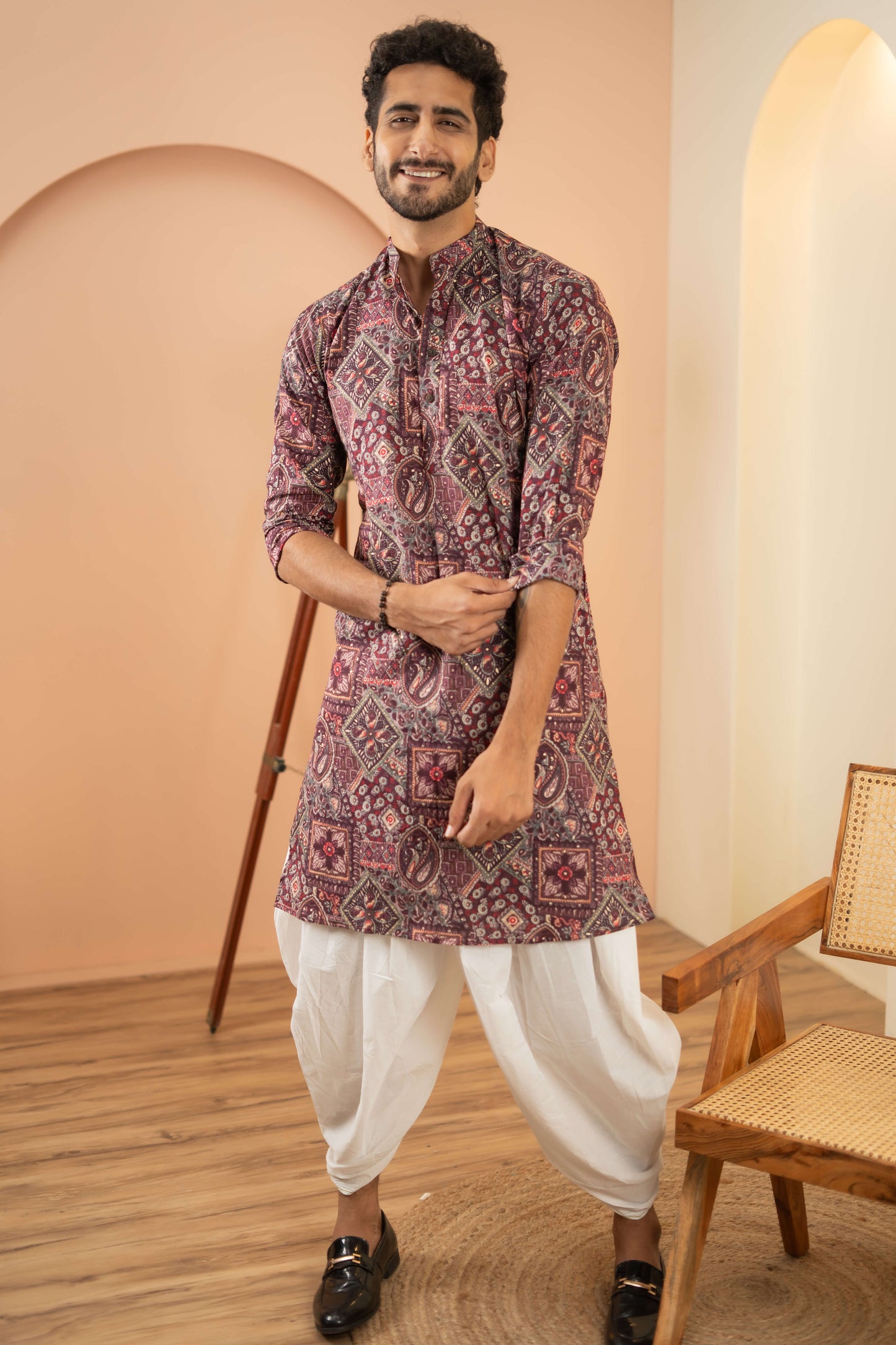 A man wearing a maroon printed kurta paired with white pants, standing confidently in a casual setting.