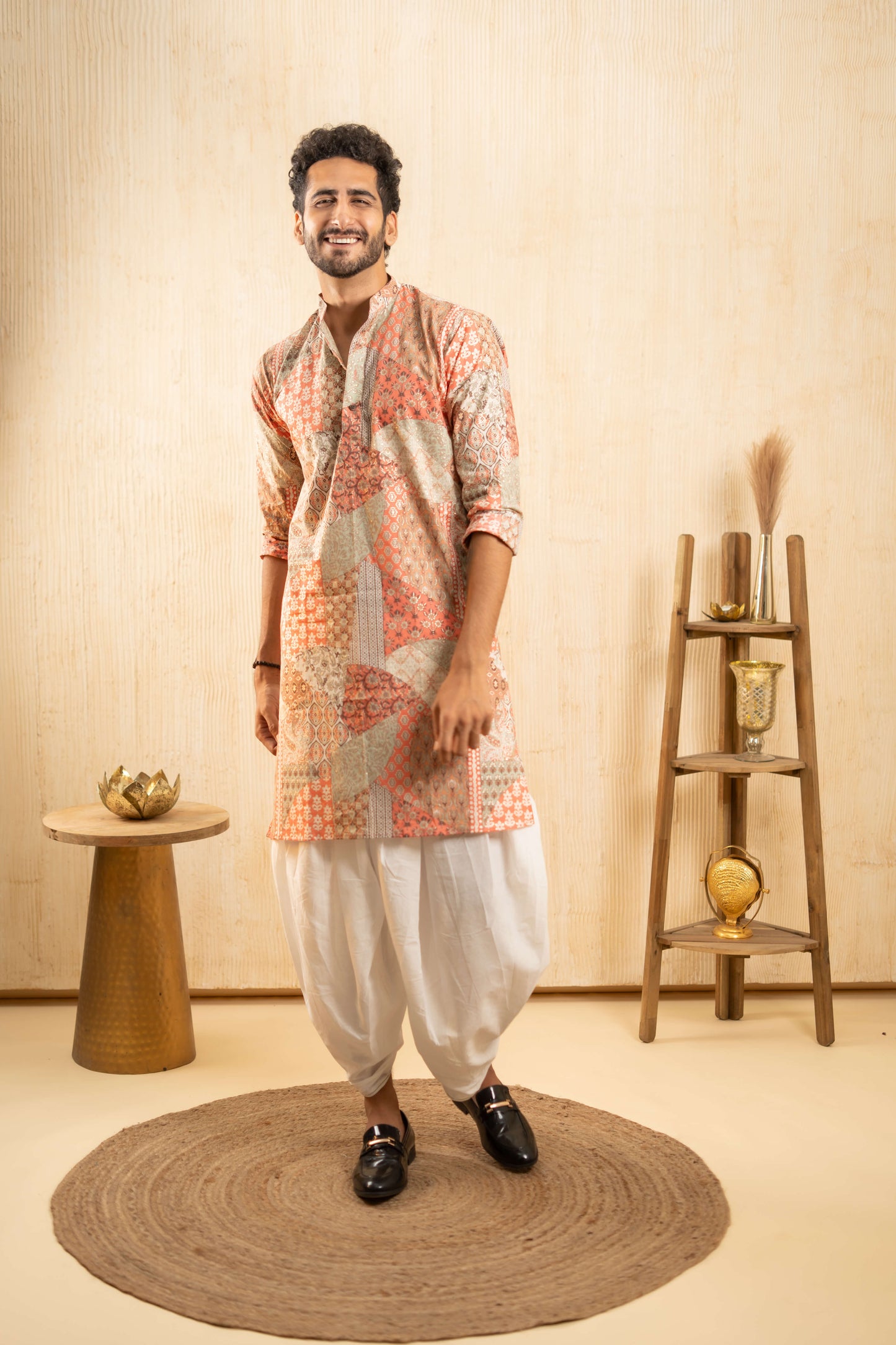 A man dressed in traditional Indian attire stands confidently in a beautifully decorated room.