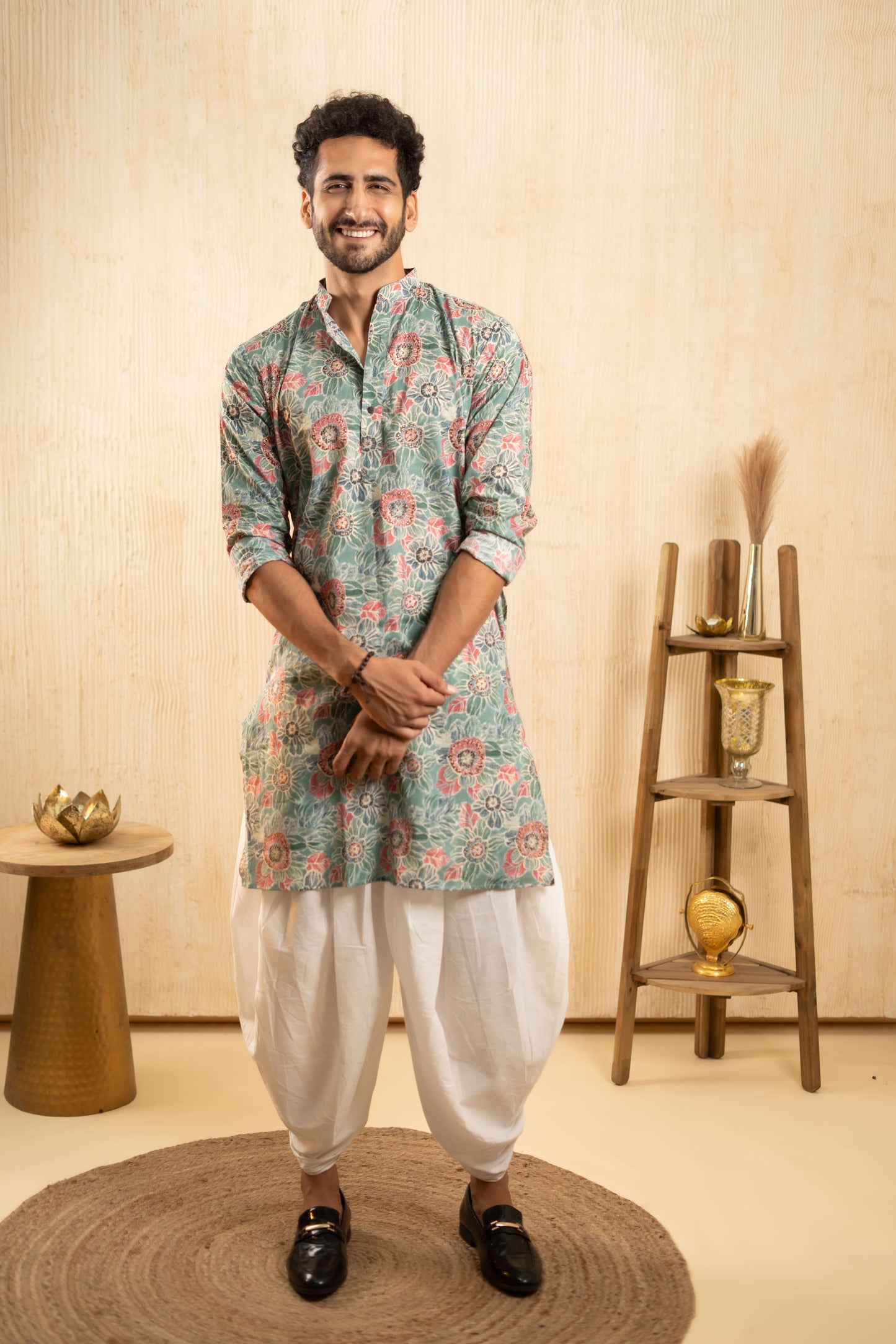 A man wearing an Indian-style outfit stands confidently in a well-decorated room.