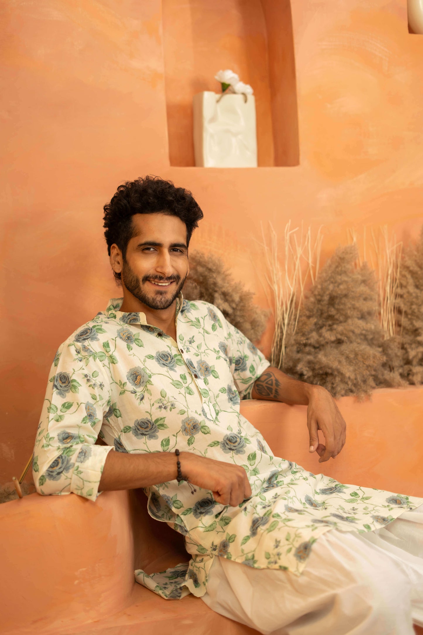 A person sits on an orange couch wearing a white floral kurta and white pants.