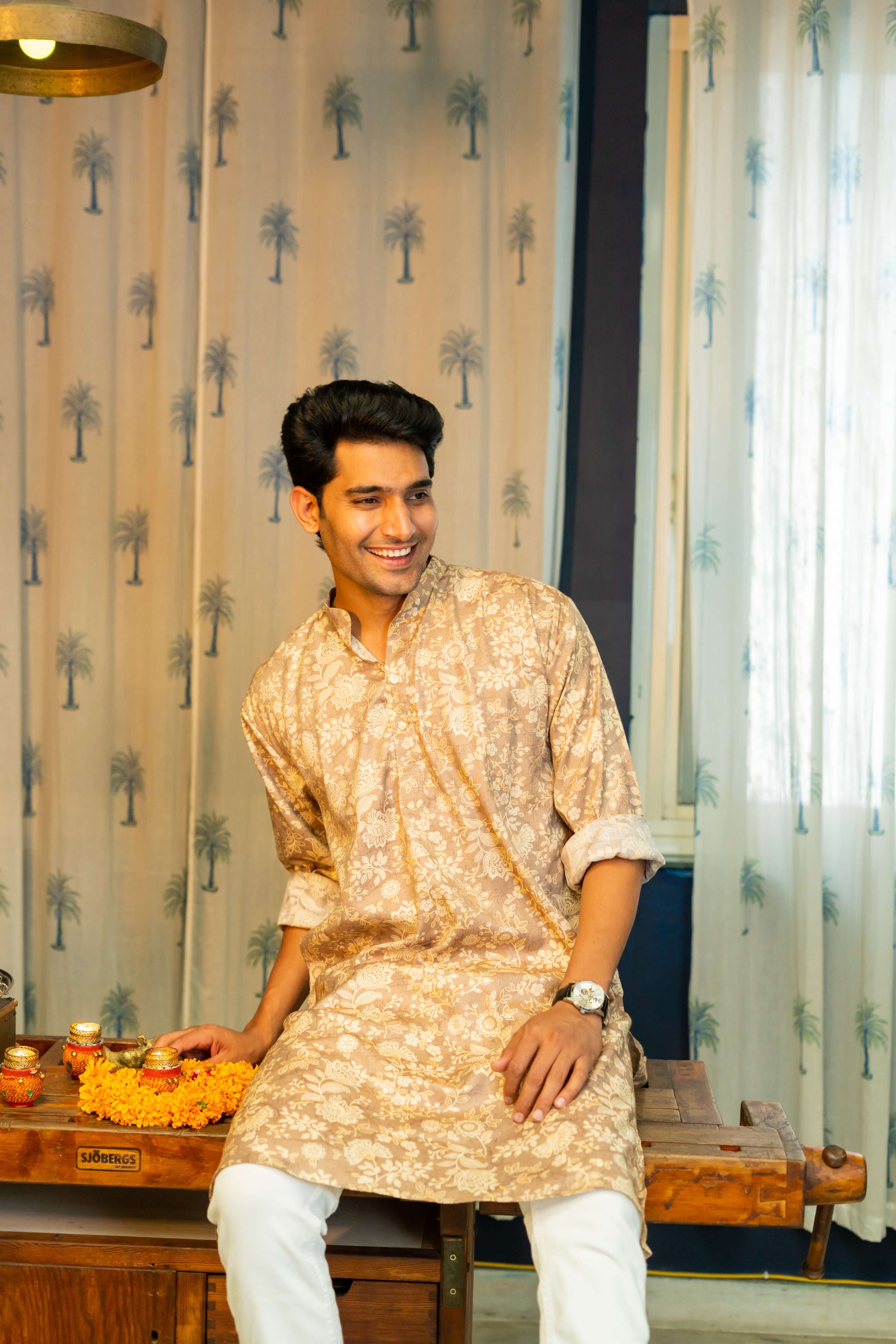 An Indian man wearing a brown color long kurta with an off-white floral print sitting on a table